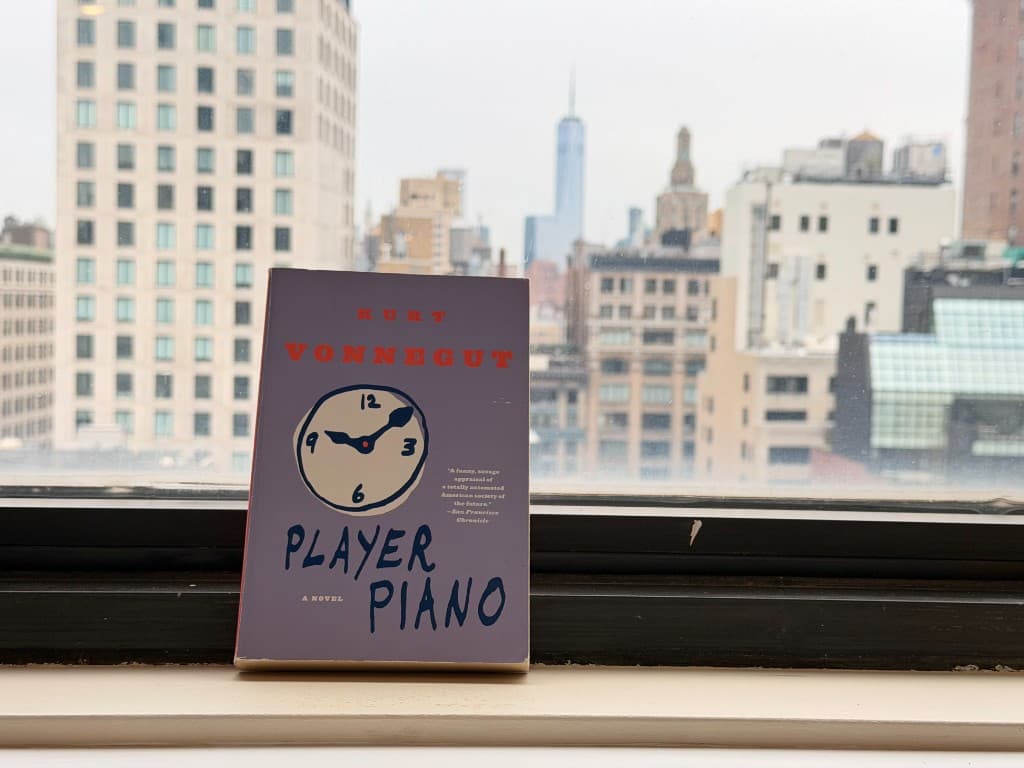 Player Piano by Kurt Vonnegut on a windowsill with a city skyline in the background